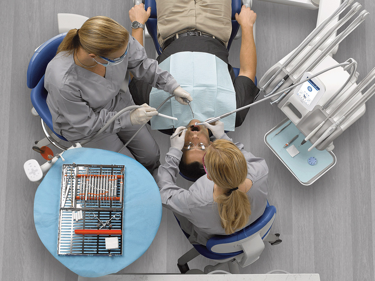 Dentist and dental assistant using a Continental-style A-dec delivery system and other tools on a patient in a chair